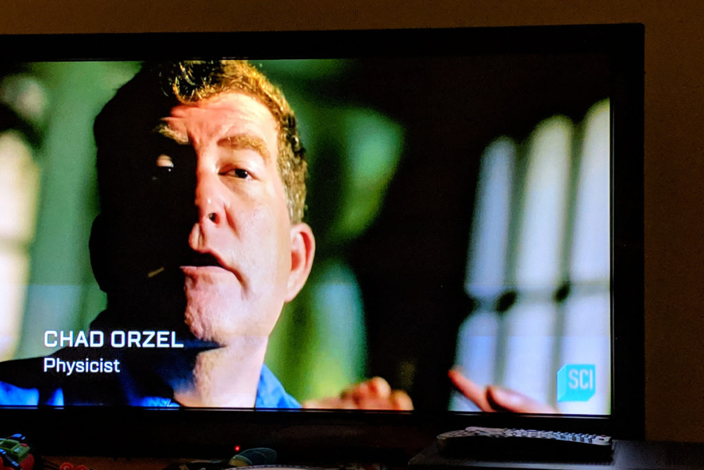 Snapshot of my face on TV, caption "Chad Orzel, Physicist"